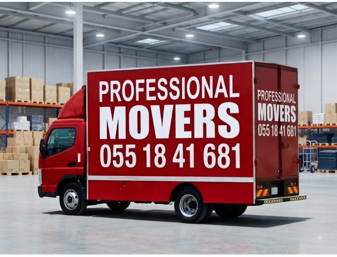 Red "Professional Movers" truck parked inside a warehouse beside stacked moving boxes.