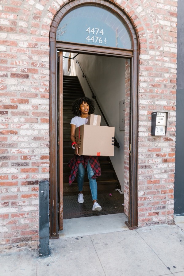 Mover carrying boxes out of an apartment building doorway.