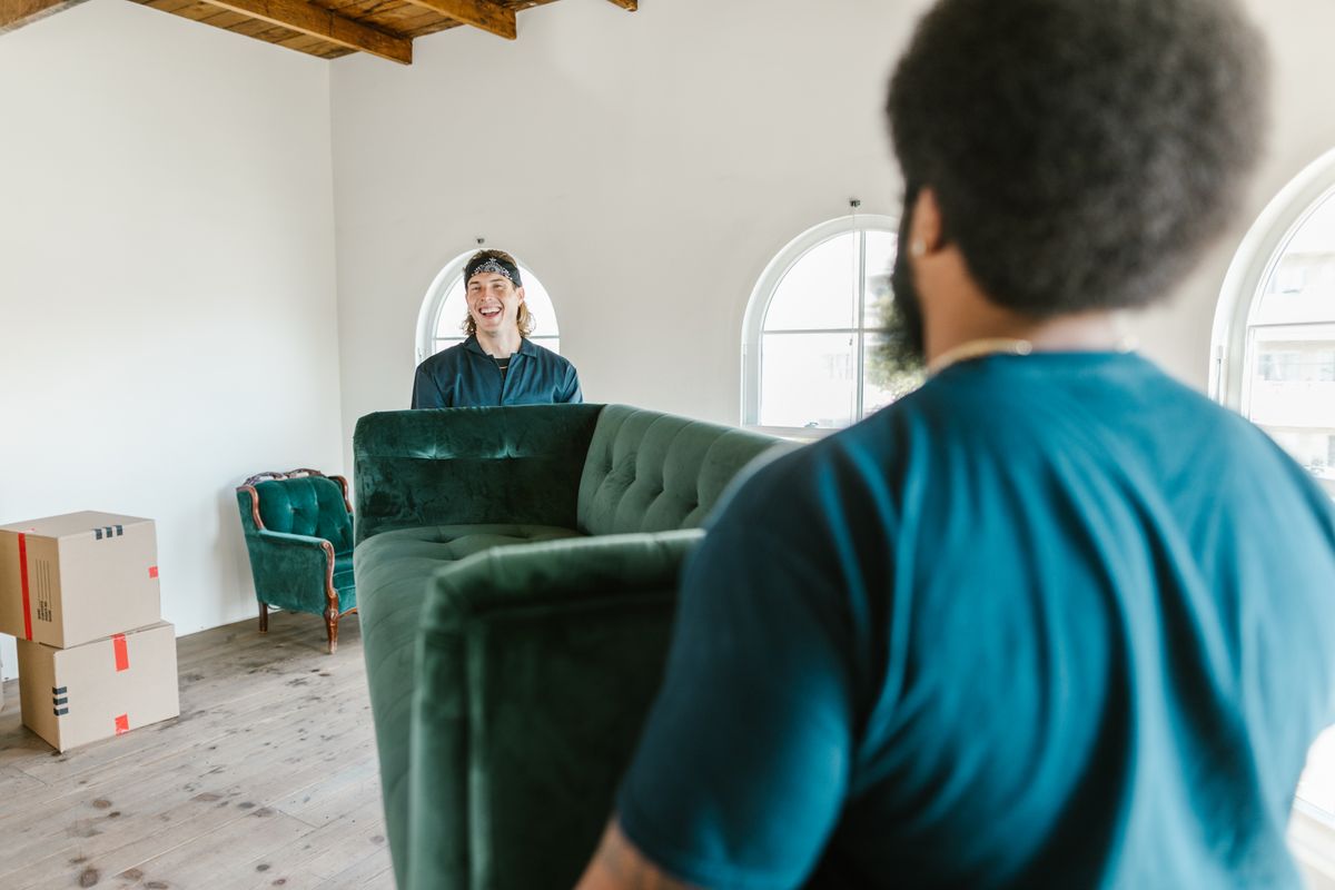 Two movers carrying a sofa into a room.